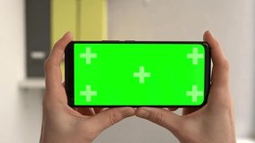 Woman hands holding green screen chroma key smartphone in office. Person using Internet, social media, online shopping with mobile phone device without keying