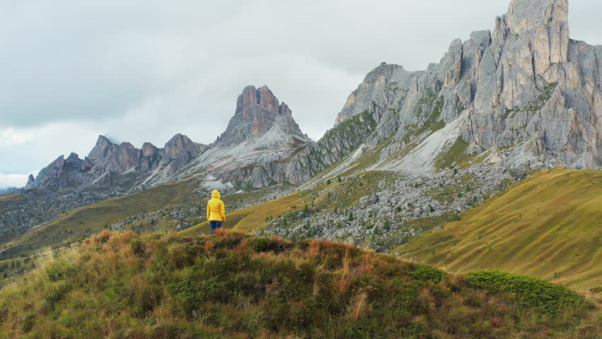 Hiker reaching hands to sky enjoys exploring mountain nature on Pass Giau. Female tourist looks around and enjoys vacation on high mountain range