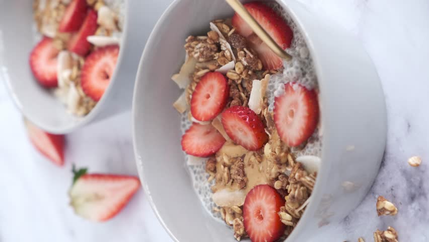 Chia pudding with homemade coconut granola, peanut butter and strawberries in a gray bowl, marble background. Healthy diet, detox, summer recipe. Royalty-Free Stock Footage #1101041803