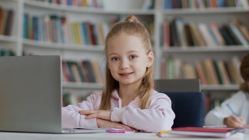 Close up portrait of cute little schoolgirl sitting at desk with laptop at school and smiling to camera, enjoying lesson in classroom interior, slow motion Royalty-Free Stock Footage #1101042319