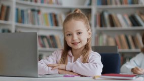 Close up portrait of cute little schoolgirl sitting at desk with laptop at school and smiling to camera, enjoying lesson in classroom interior, slow motion - Powered by Shutterstock - Get 15% off with code: PIKWIZARD15