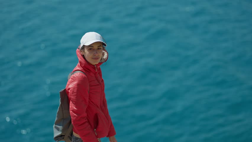 portrait of happy joyful young woman traveler in bright red jacket standing open arm at viewpoint in Antalya, Turkey. view on turquoise mediterranean sea, bay and mountain ridge
