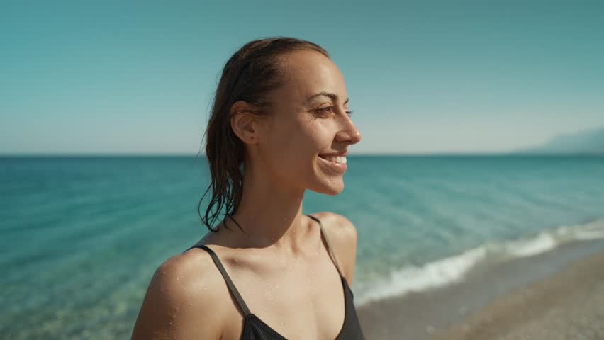Outdoor shot of smiling young female model enjoying at sea beach against blue sky. Woman having fun out on a summer day. | Shutterstock HD Video #1101044895