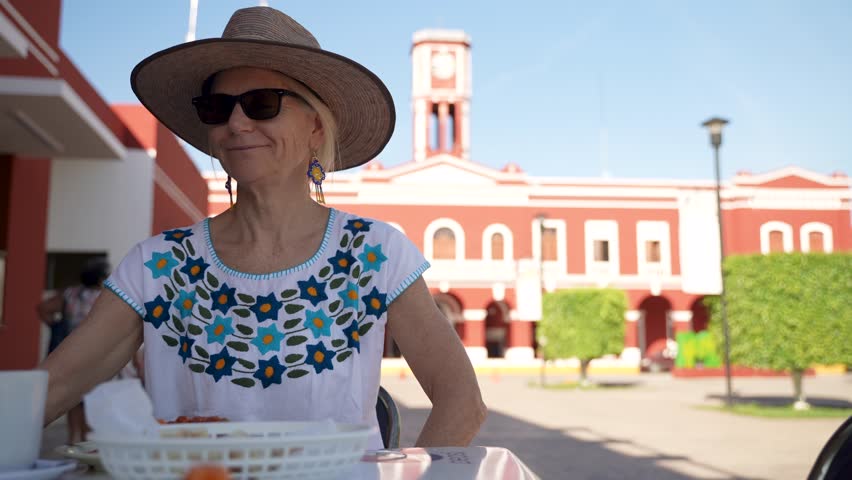 Portrait of pretty happy mature senior woman dining at a cafe in front of the Municipal Palace in Motul Yucatan Mexico with plate of huevos motulenos a local specialty dish.