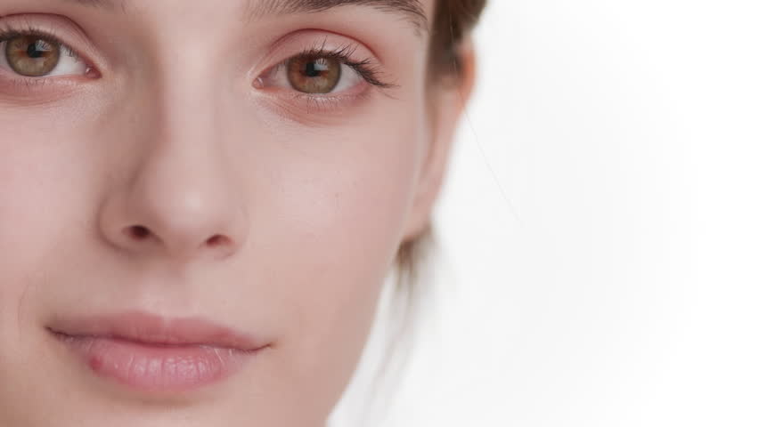 Extreme close-up shot of beautiful young brown-haired Caucasian woman with hazel eyes strokes her forehead on white background | Clean face concept Royalty-Free Stock Footage #1101045883