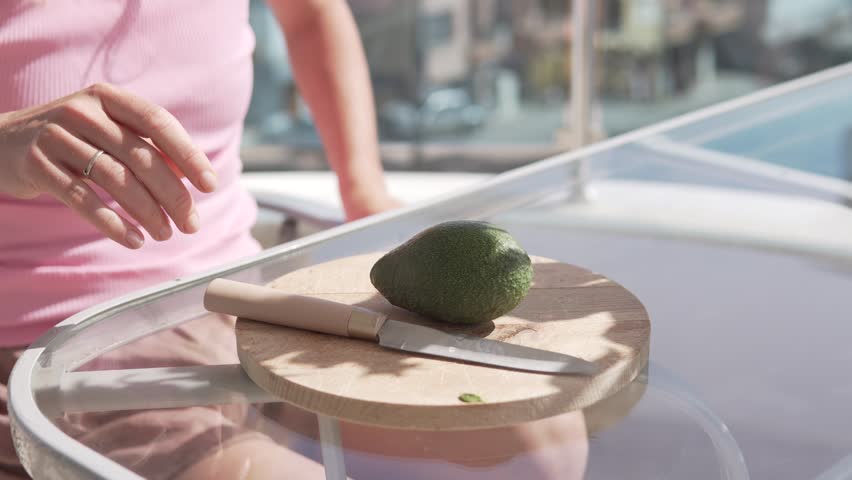 A woman cuts an avacado in half on a wooden board, close-up.