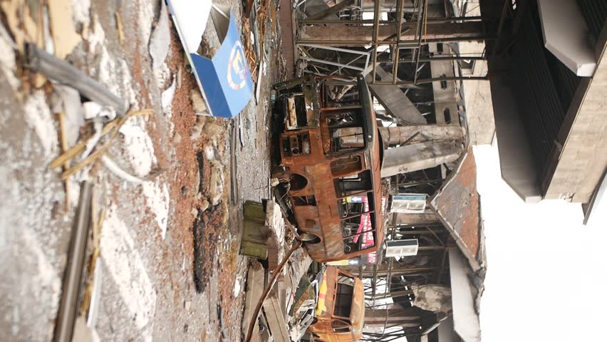 Metal frame of bus and car. Rusty body of bus and building near which transport turned into scrap metal from fire as result of shelling by rockets and bombs. War brings destruction and death