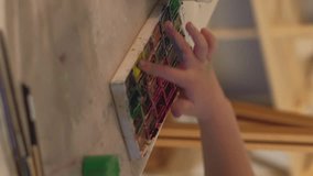 Vertical video. Kid hobby. Finger painting. Out-of-school activities. Unrecognizable talented inspired girl creating picture with watercolor paint on easel in workshop.