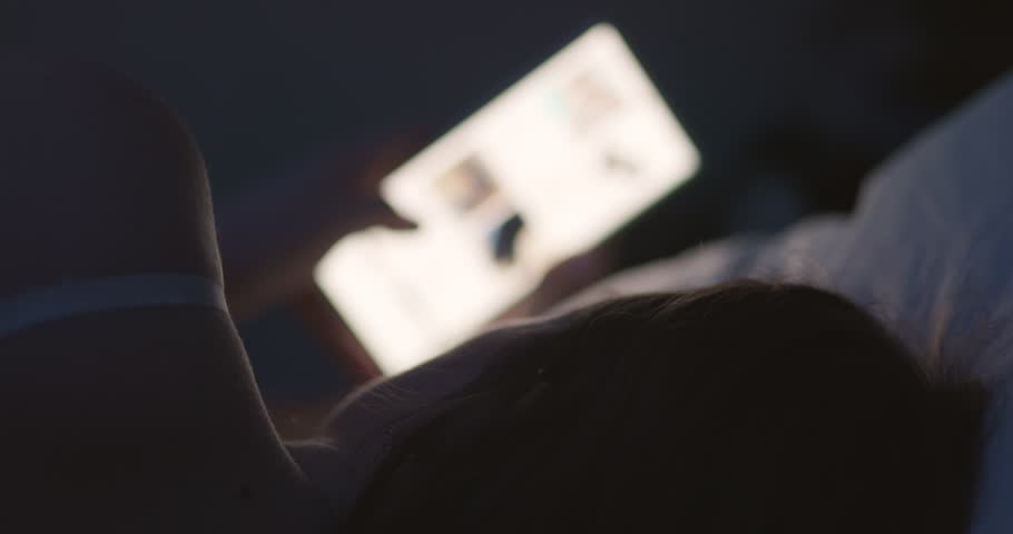 A woman lies in bed at night and uses a smartphone. Female using mobile phone Royalty-Free Stock Footage #1101052535