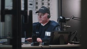 Man comes to colleague, looks view from security cameras displayed on computer and tablet monitors and talks by walkie talkie. Security officer sits at workplace and typing keyboard. CCTV technology. - Powered by Shutterstock - Get 15% off with code: PIKWIZARD15