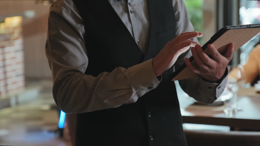 Cropped shot of waiter in elegant uniform taking order with digital tablet while working in restaurant