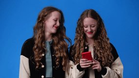 4k video of twin girls who listening music on the phone over blue background.