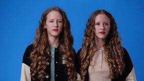 4k video of twin girls are shocked over blue background.