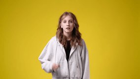 4k slow motion video of one girl counts to three and raises his hands up over yellow background.