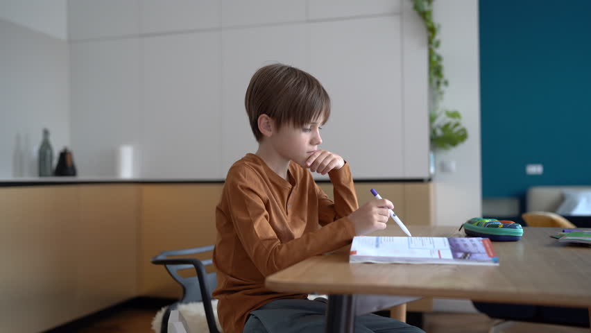 Tired upset boy sitting at kitchen table, doing homework, kid feeling depressed while studying at home, sad school-age child struggling with assignment. Homework anxiety in kids, learning disorders | Shutterstock HD Video #1101055201