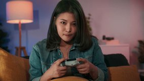 Excited beautiful Asian woman using joystick wireless controller enjoy playing console video game to win highest victory. Gamer emotion expression smile focused on the match. Hand held Video shot