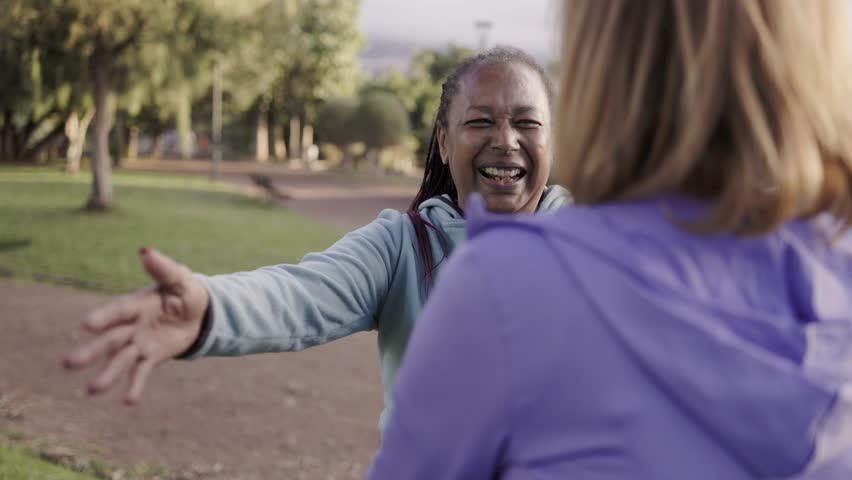 Multiethnic senior women hugging and meeting outdoors at park city - Elderly lifestyle community concept