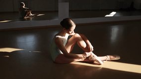 Tender teen girl, classical ballet dancer getting ready to train in ballet school on a daytime with sunlight. Putting on pointe shoes. Concept of ballet, dance art, education, beauty, choreography