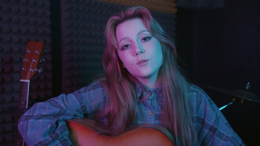 Young pretty woman playing guitar in the sound recording studio