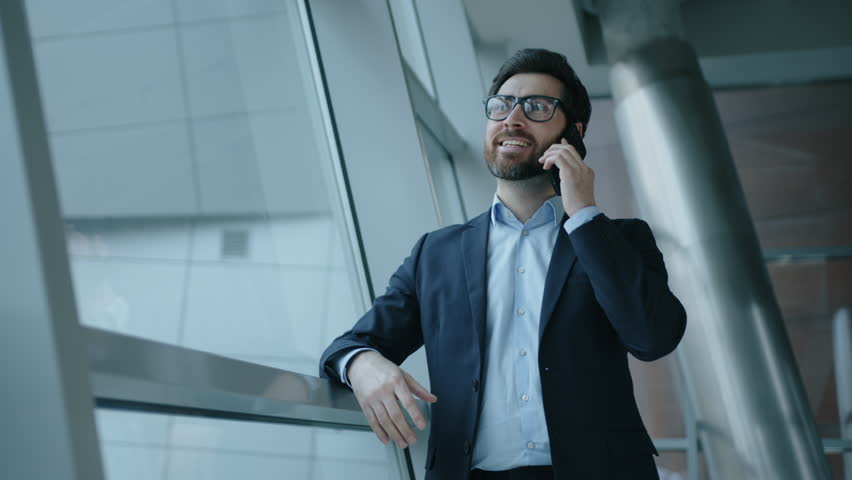 Close-up shot of a smiling, happy, bearded man standing by the window. Portrait of caucasian man in formal suit having a business call in modern office. High quality 4k footage Royalty-Free Stock Footage #1101061121