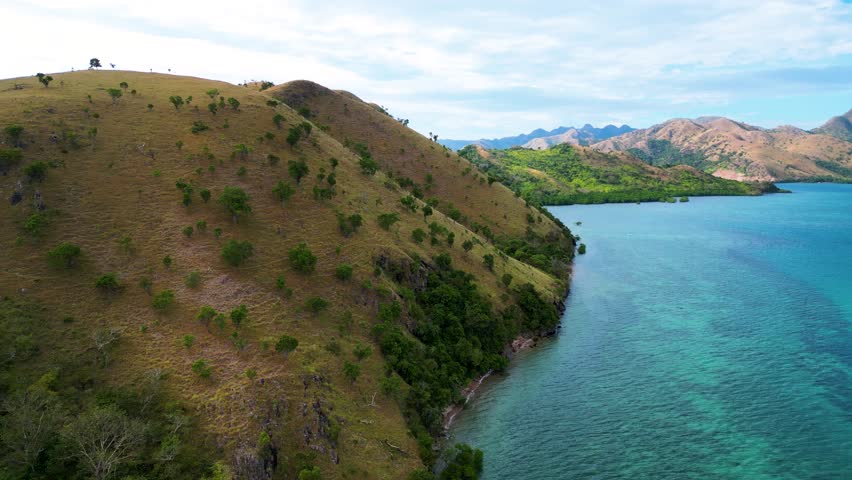 Unique brown hills with some green bushes and trees, blue water with patches of bright turquoise green on a sunny summer afternoon in Coron, Philippines