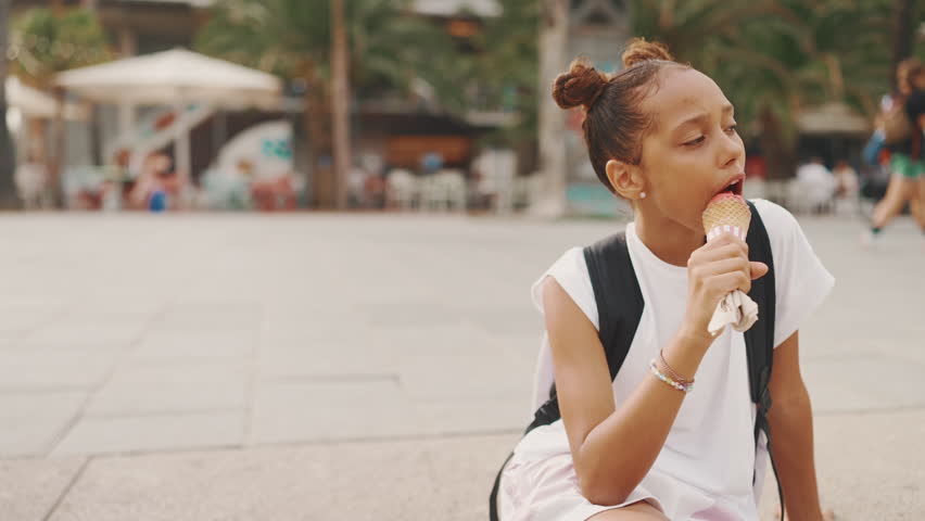 Pre-teenage girl enjoys ice cream sitting on the embankment with her legs dangling from the pier