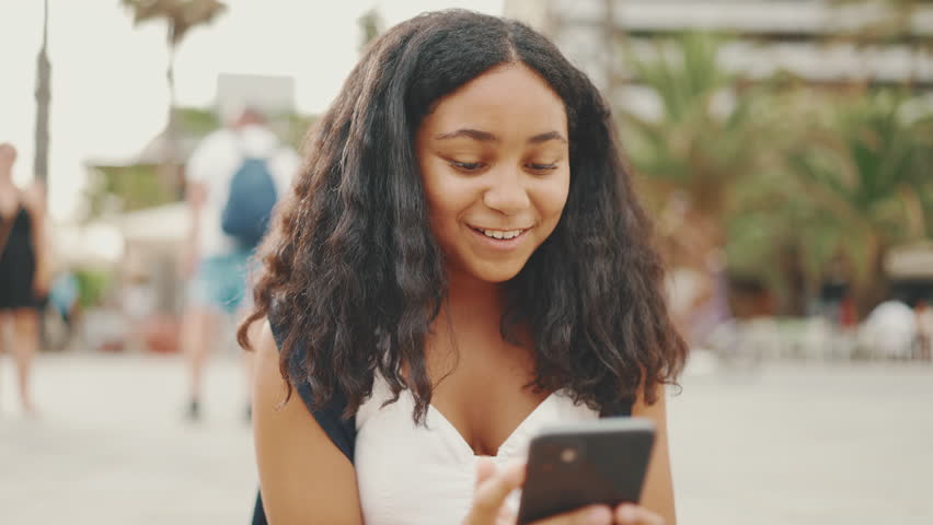 Pre-teenage girl uses mobile phone while sitting on the waterfront. Teenage girl making video call on smartphone | Shutterstock HD Video #1101067327