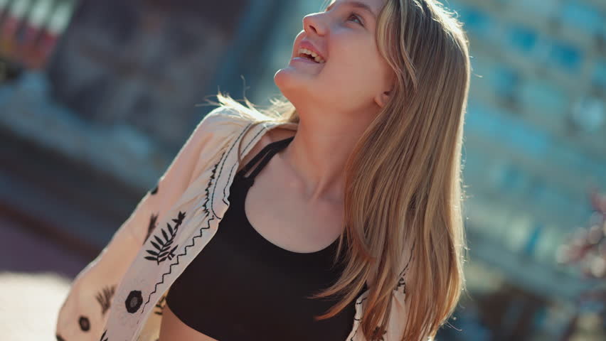 Happy teenage girl in sunrays with live camera spinning zoom in. Portrait of positive beautiful teenager smiling looking around standing on city street