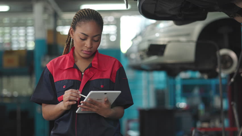 Afican engineer checking under car condition on lifter in garage.Young auto mechanic in uniform is looking at camera and smiling examining car. Royalty-Free Stock Footage #1101070881