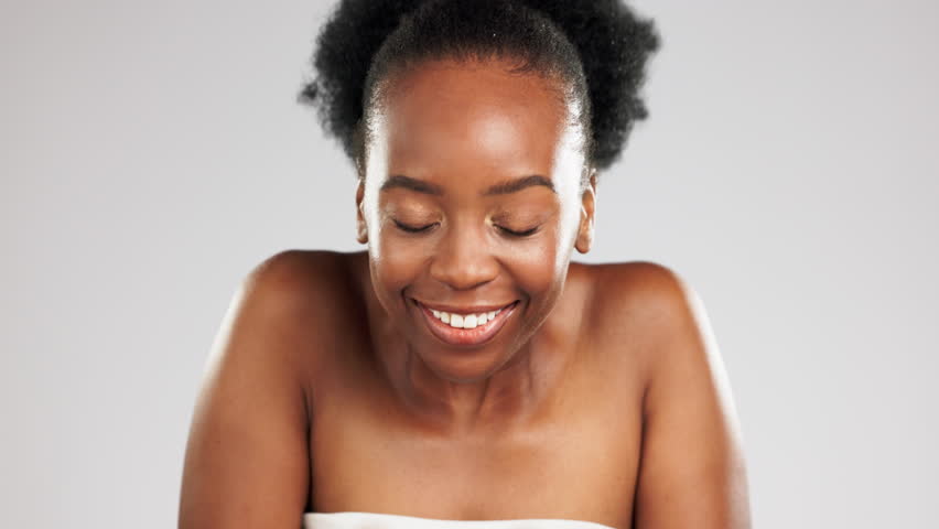 Face, skincare and water splash of happy black woman in studio isolated on a gray background. Cleaning portrait, cosmetics bubbles and laughing female model apply lotion, cream or skin moisturizer. Royalty-Free Stock Footage #1101072693