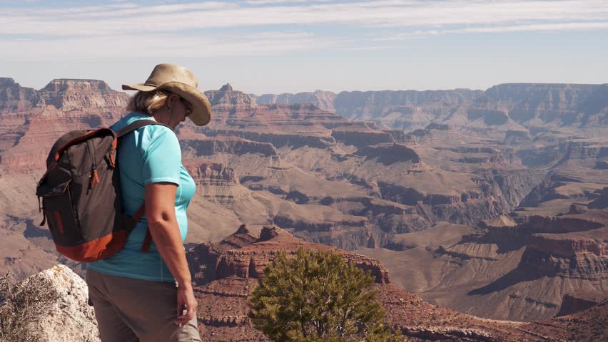 Stunning nature of great Grand Canyon in National Park. Female hiking tourist with backpack walking edge at top of observation deck and enjoys views of red rocks and canyon gorges from height Royalty-Free Stock Footage #1101079043