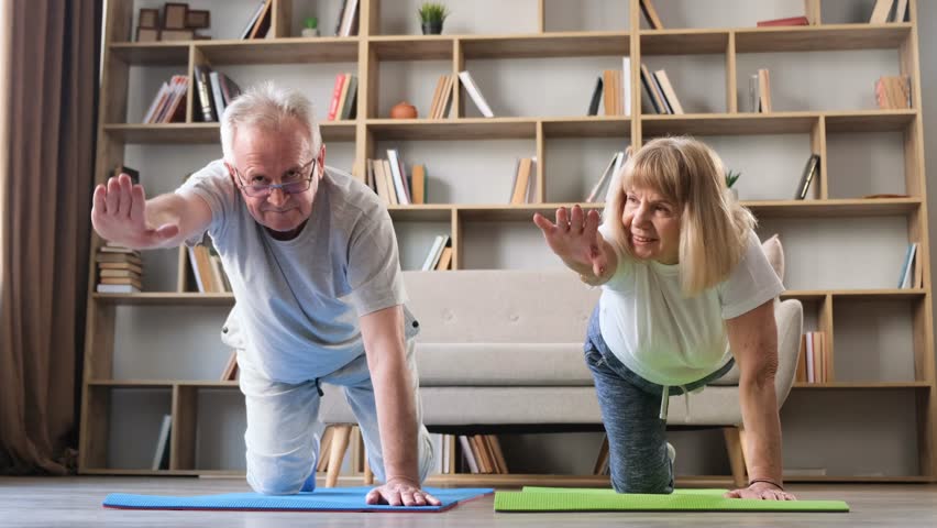 Grandparents doing gymnastics and yoga at home in the living room, sunny morning.  Royalty-Free Stock Footage #1101081443
