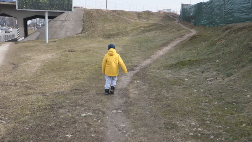 boy in a yellow jacket and hat walks the streets of a small town