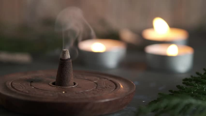 An incense cone burning and generating aromatic smoke surrounded by small candles | Shutterstock HD Video #1101084593