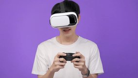 Asian young man in white t-shirt and playing video games using joysticks with headphones on voilet background isolated.