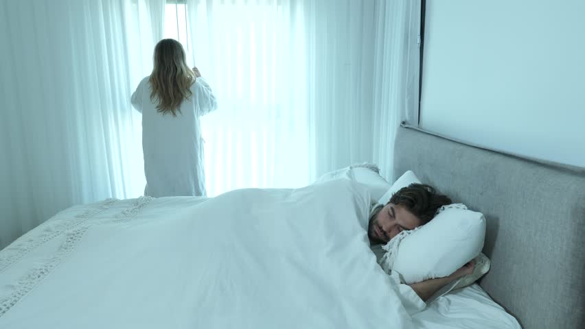 Adorable blond woman wake up man by opening window curtain, honeymoon concept Royalty-Free Stock Footage #1101088451