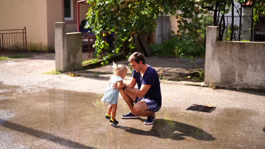 Little girl with her dad jump through the puddles in the yard Royalty-Free Stock Footage #1101089087