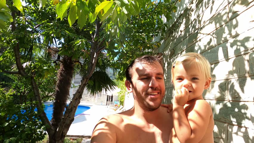 Dad with a little girl in his arms walks through the garden near the house