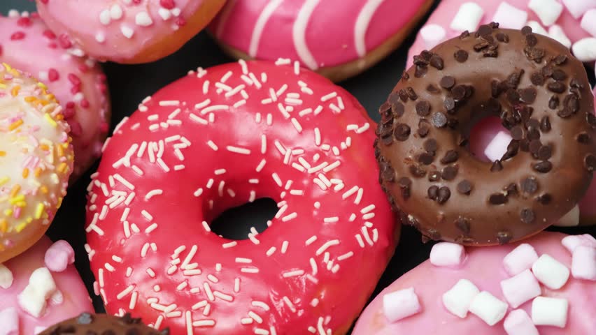 Donuts with red, pink and chocolate icing and marshmallows spin the view from above Royalty-Free Stock Footage #1101093321