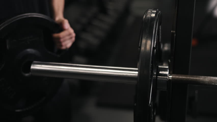 Fitness equipment, Gym equipment, Muscle endurance. Gym-goer is shown loading up his barbell with additional weights.
