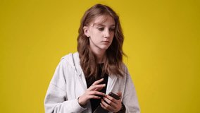 4k video of one girl who thinking about something while holding the phone and playing with his hands over yellow background.
