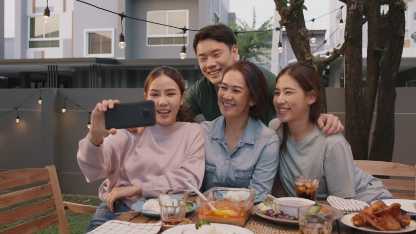 Young adult asia people hug love care for mom taking photo selfie video on mobile phone camera at home picnic dining fun night party dine table. Relax older mum smile enjoy warm time happy hour meal. Royalty-Free Stock Footage #1101104195