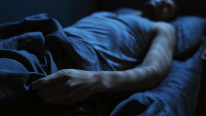Selective focus of young military man suffering post-traumatic stress disorder squeezing blanket while having nightmare