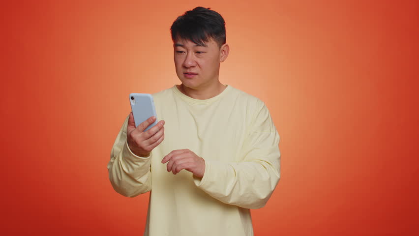 Asian happy man using smartphone pointing empty place, advertising area for commercial text, mobile application, promotion copy space, recommends wifi cellular connection 5G. Handsome chinese guy