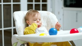 Infant playing with balls, sitting in a special chair, not to follow down. Toddler leisure activity while mother cooking meal.