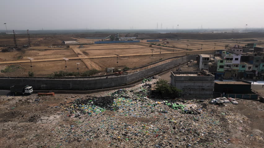 Aerial panning shot showing dumping ground next to residential buildings in the suburbs of Mumbai, Maharashtra, India. Environmental issues, poverty and overpopulation concept.