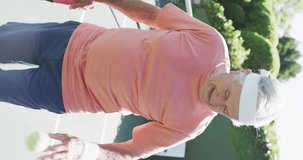 Vertical video of portrait of happy senior caucasian man laughing in tennis court, in slow motion. Healthy, active senior lifestyle.