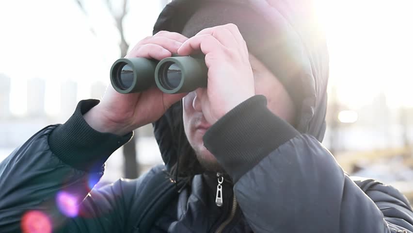 A man rests outside the city looking through binoculars and watching birds