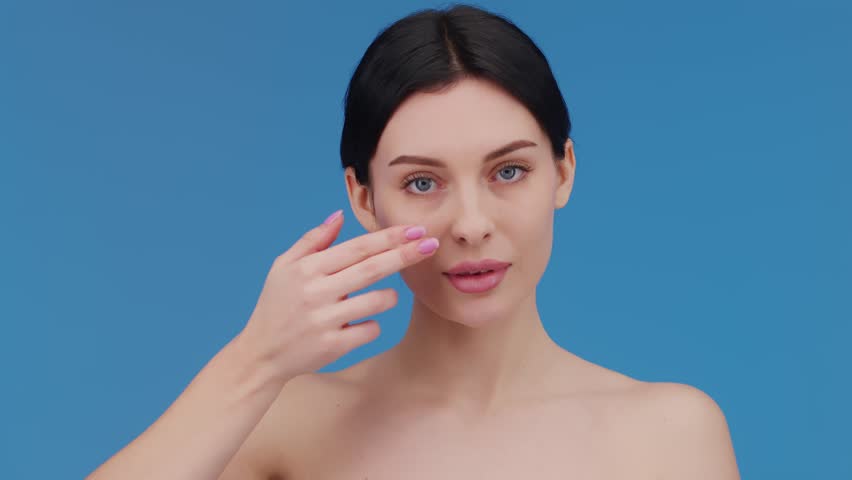 Beautiful woman applying moisturizer to her face. Video of a smiling woman with perfect makeup on a blue background. Beauty concept
 Royalty-Free Stock Footage #1101113839