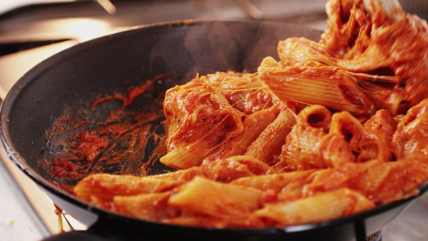 Chef cooking penne pasta with tomato sauce and mozalerra cheese in pan, close up. Cooking traditional italian cuisine, food in Italy.